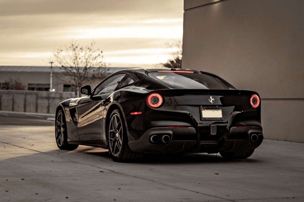 A sleek black sports car, recently treated with a ceramic coat, is parked on a sunlit concrete surface. Its taillights glow red against a subtle evening sky.