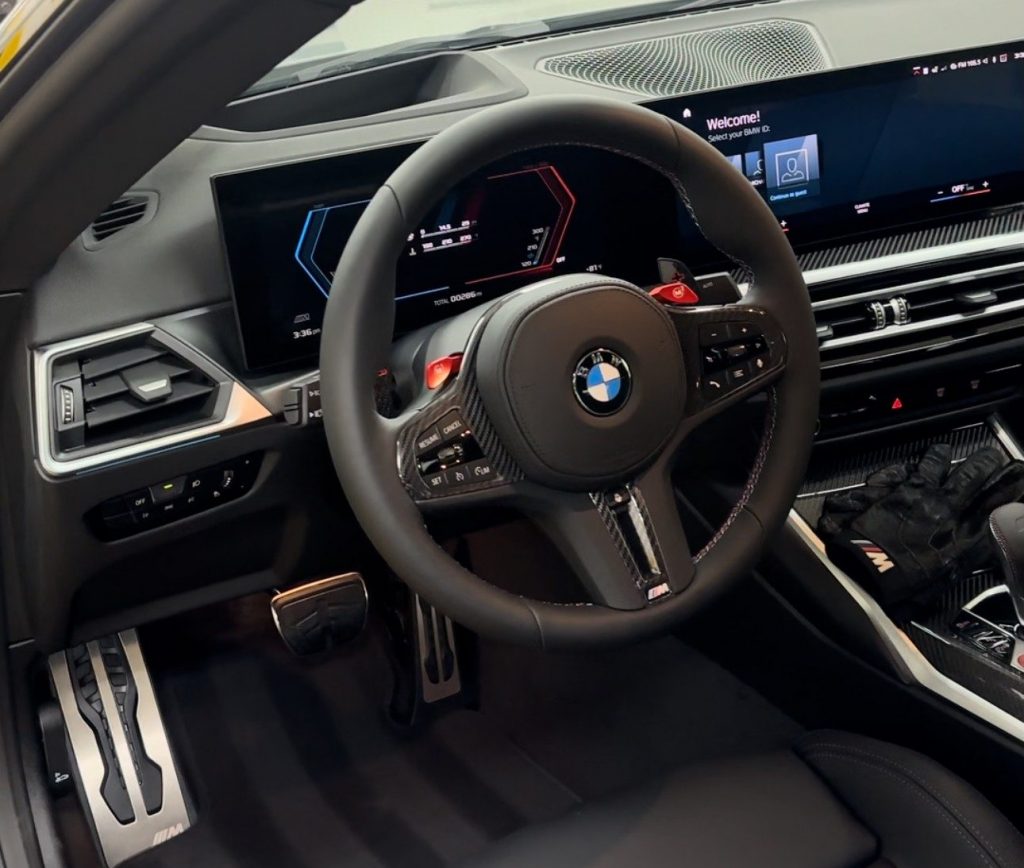 The interior of a BMW car showcases a sleek steering wheel with red paddle shifters, modern digital dashboard displays, and an immaculate black leather finish. The center console and foot pedals are also visible, reflecting the meticulous attention to an interior clean.